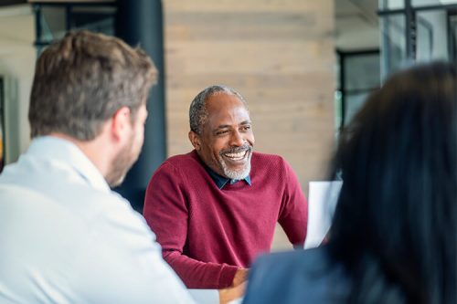 smiling man in red sweater sits with colleagues at conference table