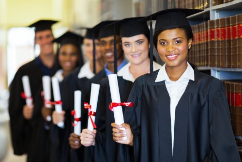 A line of students hold their diplomas in a library