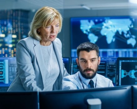 Information technology professionals at work in a room filled with monitors.