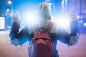 Juvenile holds hands up at night in the city, with police lights shining.