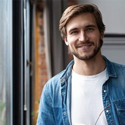 A young man in a denim shirt standing in front of a window, while pursuing an online masters degree in AI.