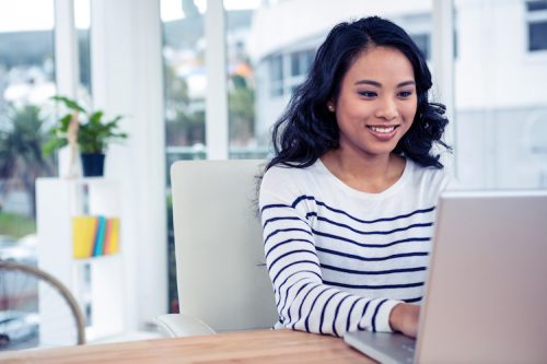 A young Asian woman sitting at a desk using a laptop to pursue her online master's in AI