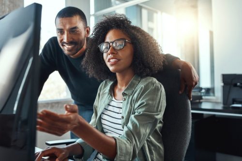 Two individuals collaborating on a computer in an office while pursuing their online masters in AI.