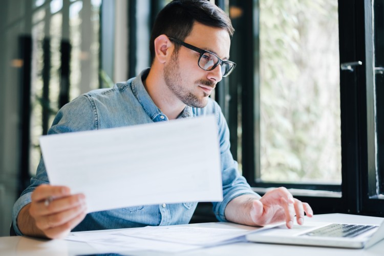 A data scientist holds a printout while working on a laptop.