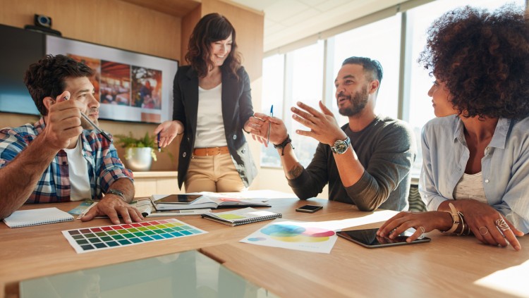 An advertising manager leads a meeting with colleagues at a conference table.