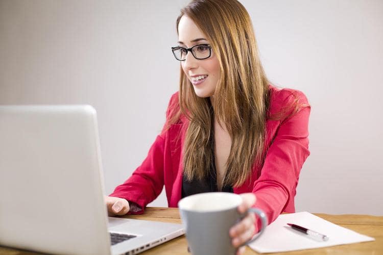 Lady at a desk with one hand on a laptop and her other hand on a cup