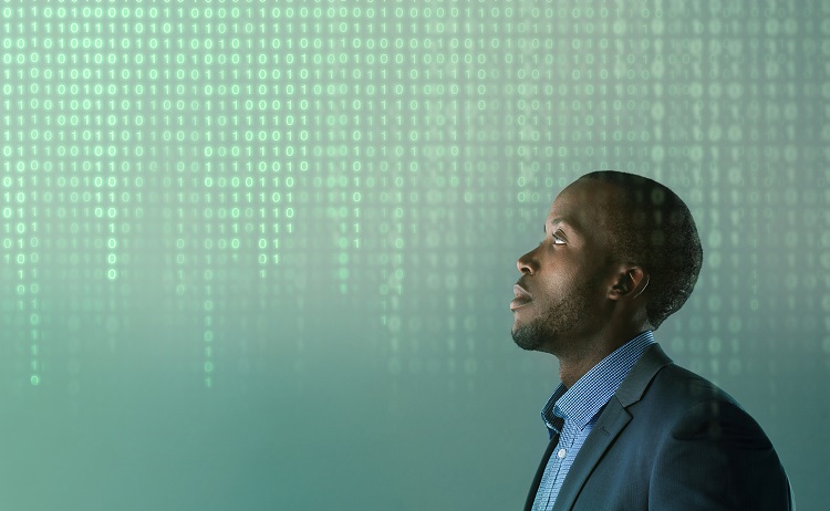 A man in a suit jacket looks up at a grid of digital binary numbers