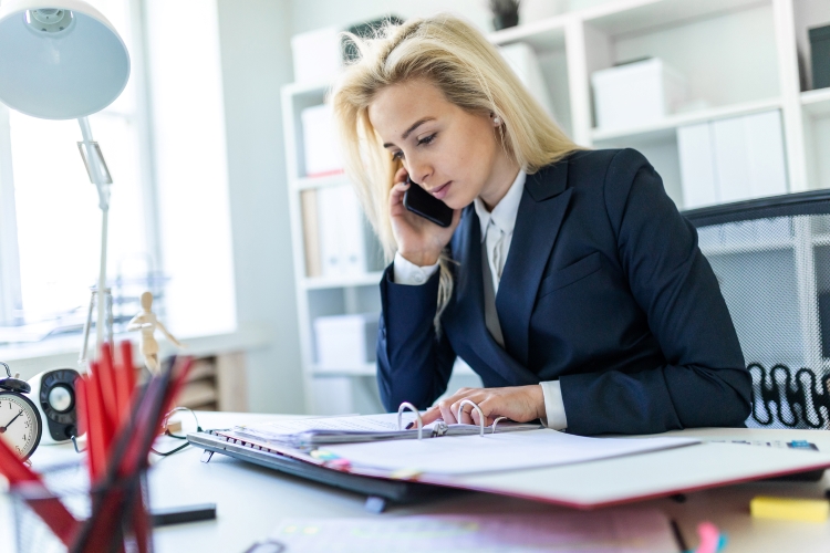 An insurance underwriter reviews documents while talking on her cell phone.