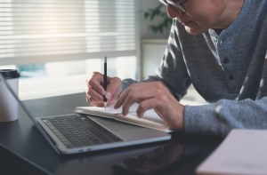 An online education student takes notes while working on a laptop.