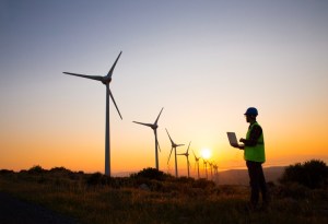 A wind turbine technician works onsite with a laptop.