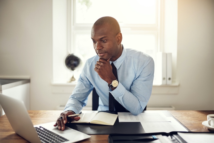 An accountant sits at his desk, working on his laptop and reviewing papers