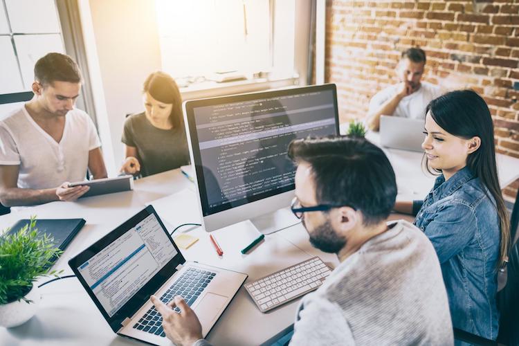 group of network analysts analyze each other’s screens around a table in an office space