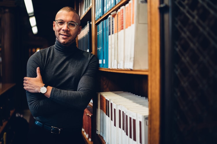 Archivist poses in library aisle by books.