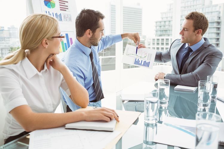 three people sitting around a table discussing graphs and numbers