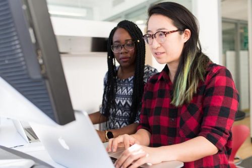 two females with glasses using their laptops