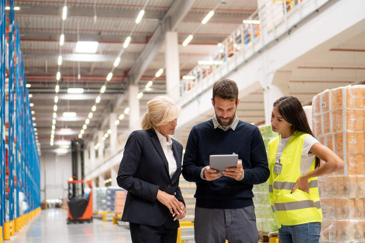 Two managers and a warehouse worker look at current inventory on a tablet 