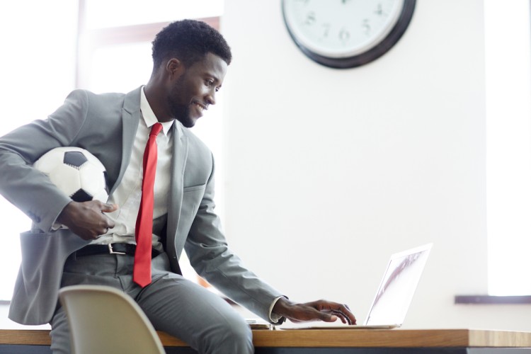 A sports executive holding a soccer ball works on a laptop.