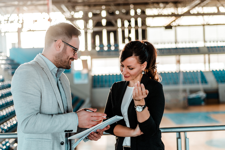 Two sports managers review sport business documents in a gymnasium.