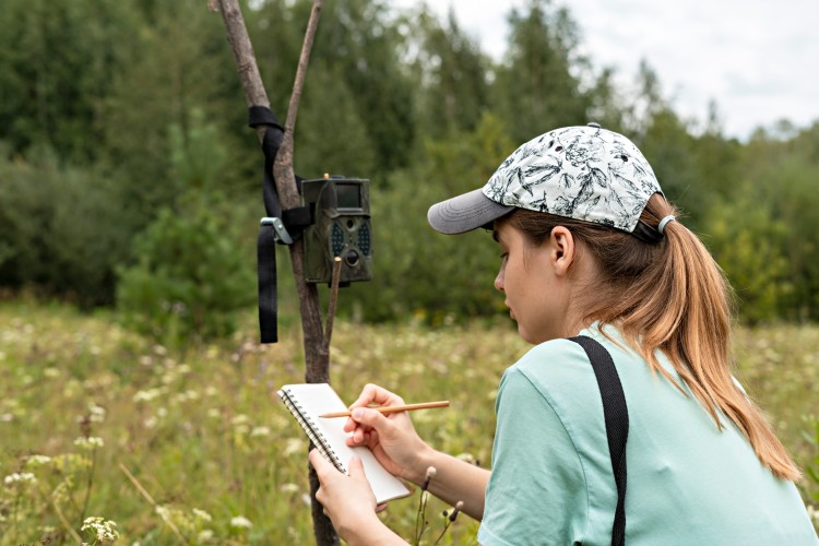 Wildlife biologist observing an ecosystem and writing in a notebook. 