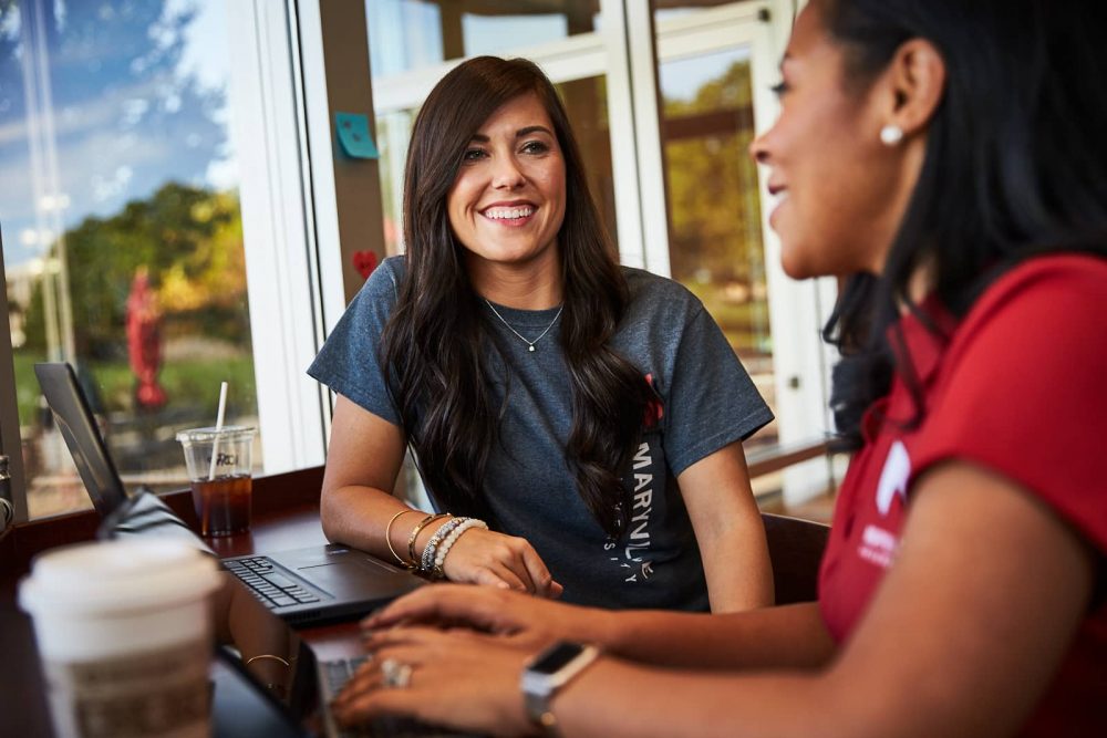 A student with a laptop talks with an advisor.