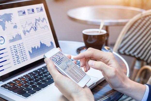 A fintech professional uses a laptop and phone to monitor financial data.