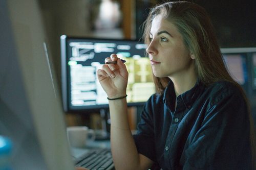 woman holds pen and looks at computer screen