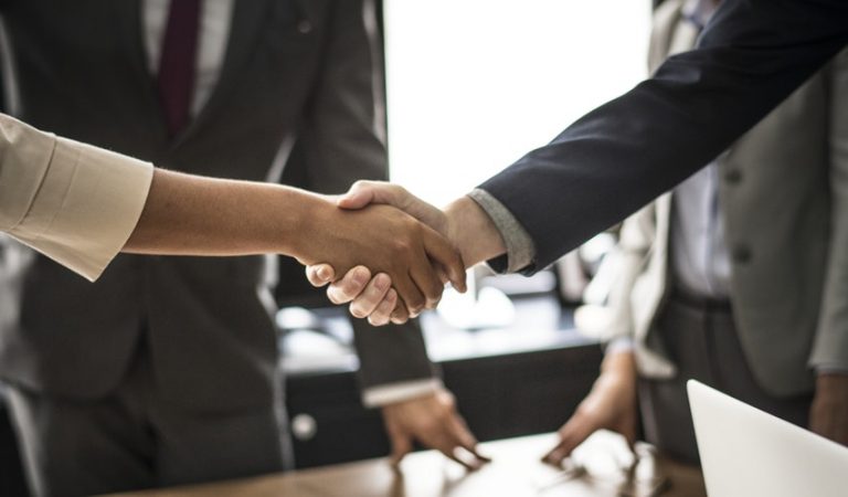 Two persons are shaking hands in a meeting. 