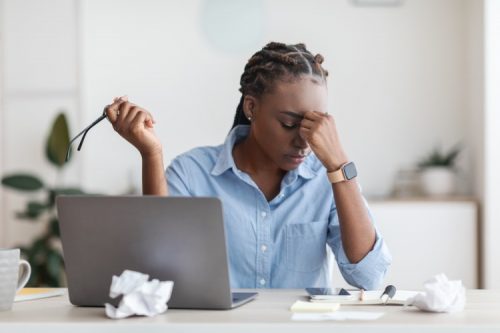 A stressed student holds her forehead while working on a laptop.