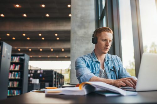 Student studying in a library with headphones on.